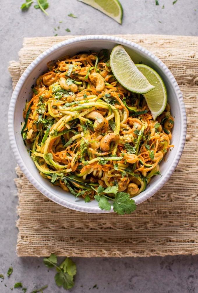 Eine appetitliche Schüssel Knoblauch-Limetten-Cashew-Zoodles, garniert mit frischen Limettenspalten, die auf einer Oberfläche präsentiert wird.