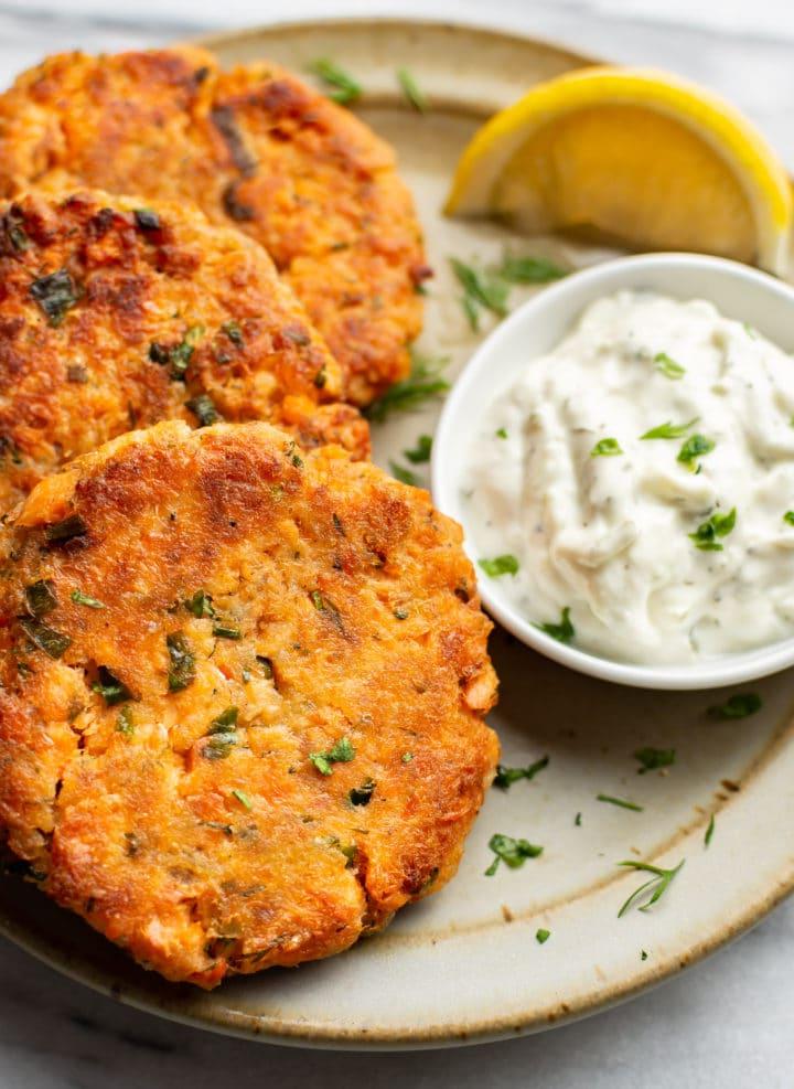 Ein Teller mit drei Lachs-Patties, einer Zitronenspalte und Dip