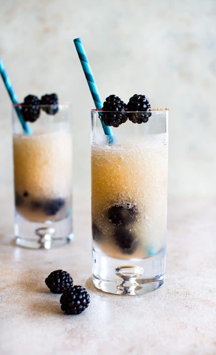 Zwei klare Gläser mit gefrorenem Brombeer-Riesling und blau gestreiften Papierstrohhalmen, garniert mit frischen Brombeeren