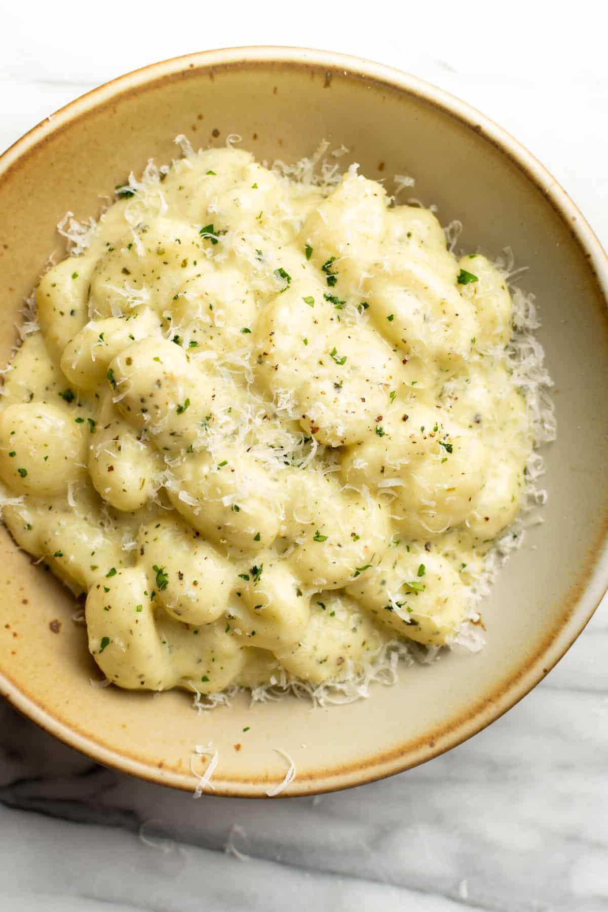 Eine Schale mit cremigen Pesto Gnocchi, garniert mit frischem Basilikum und geriebenem Parmesan.