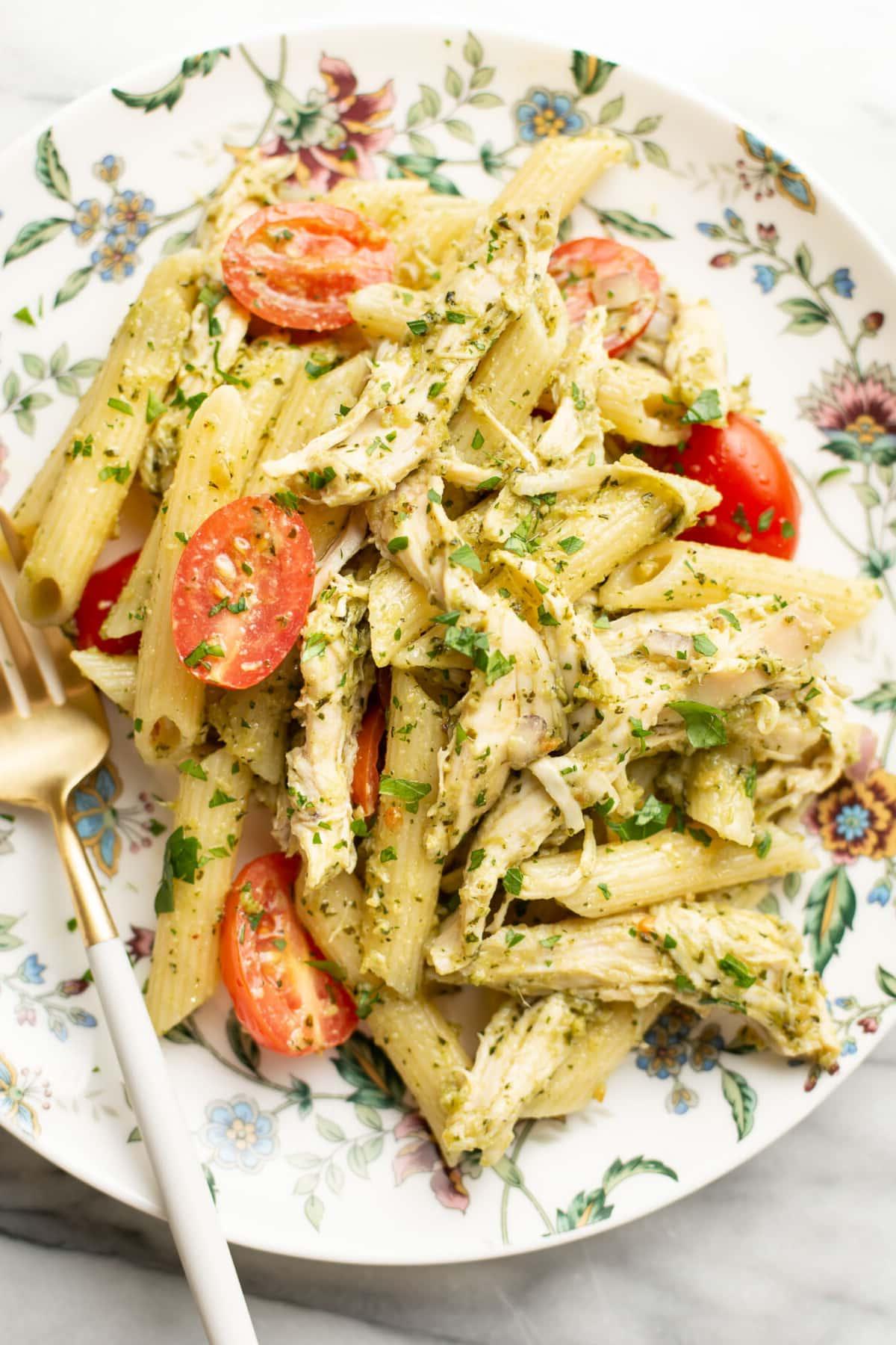Ein Teller mit Hähnchen-Pesto-Nudelsalat und einer Gabel, appetitlich angerichtet.