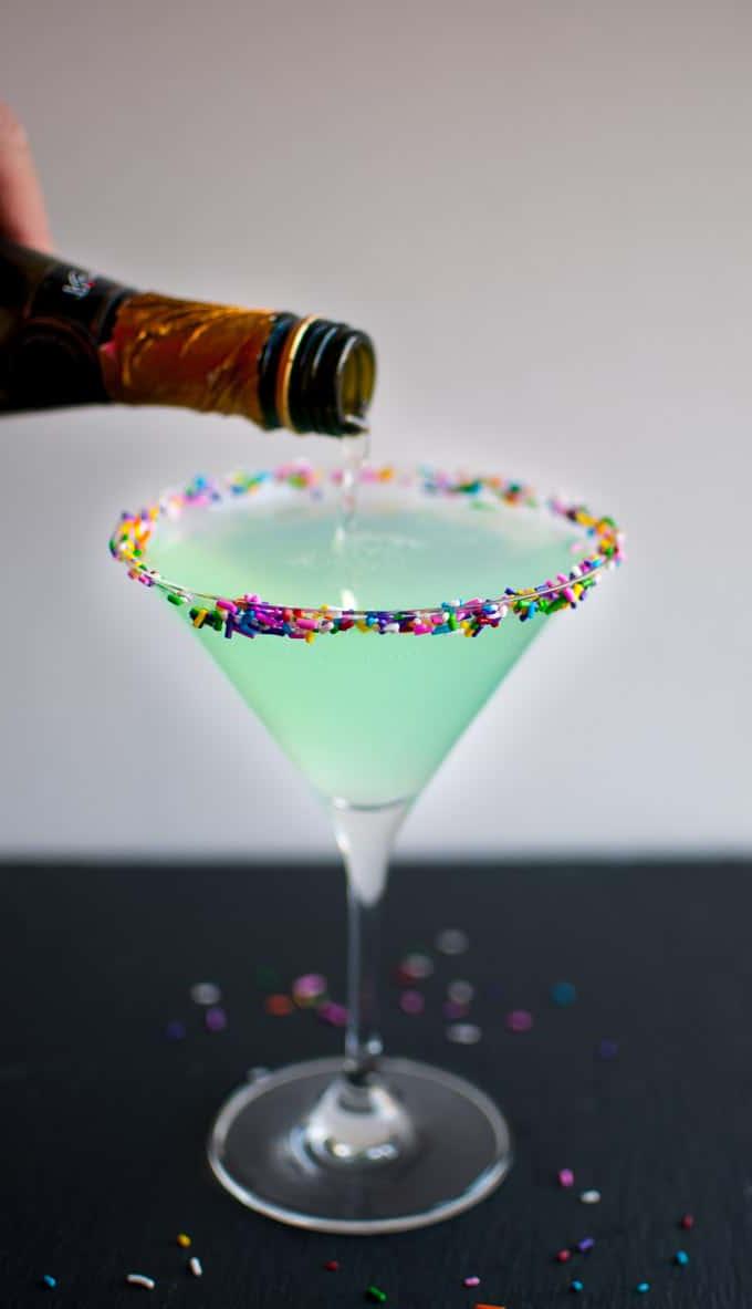 Martini-Glas mit Sprinkletini, in das Champagner gegossen wird