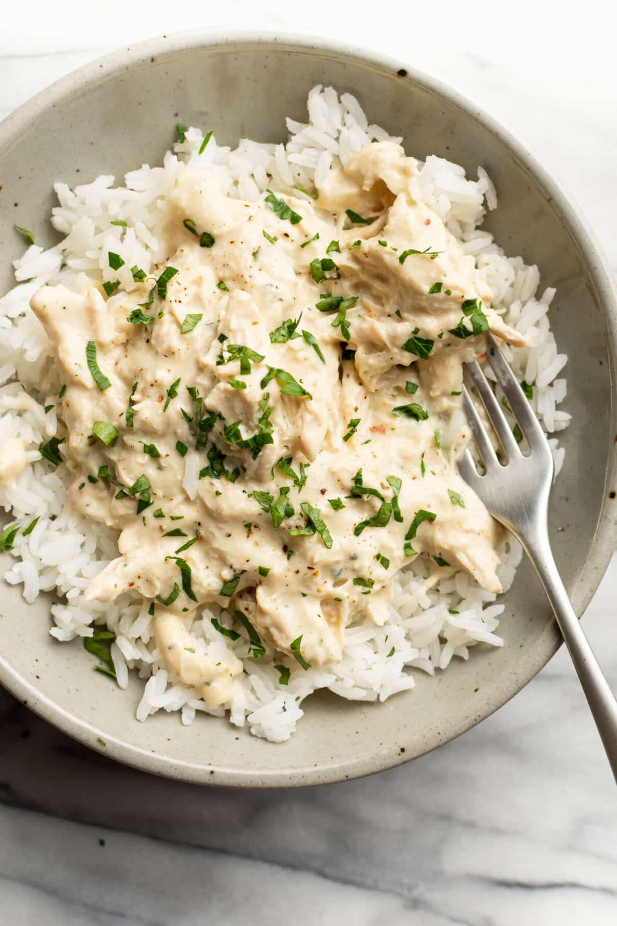 Eine Schale mit italienischem Hähnchen aus dem Slow Cooker über Reis mit einer Gabel