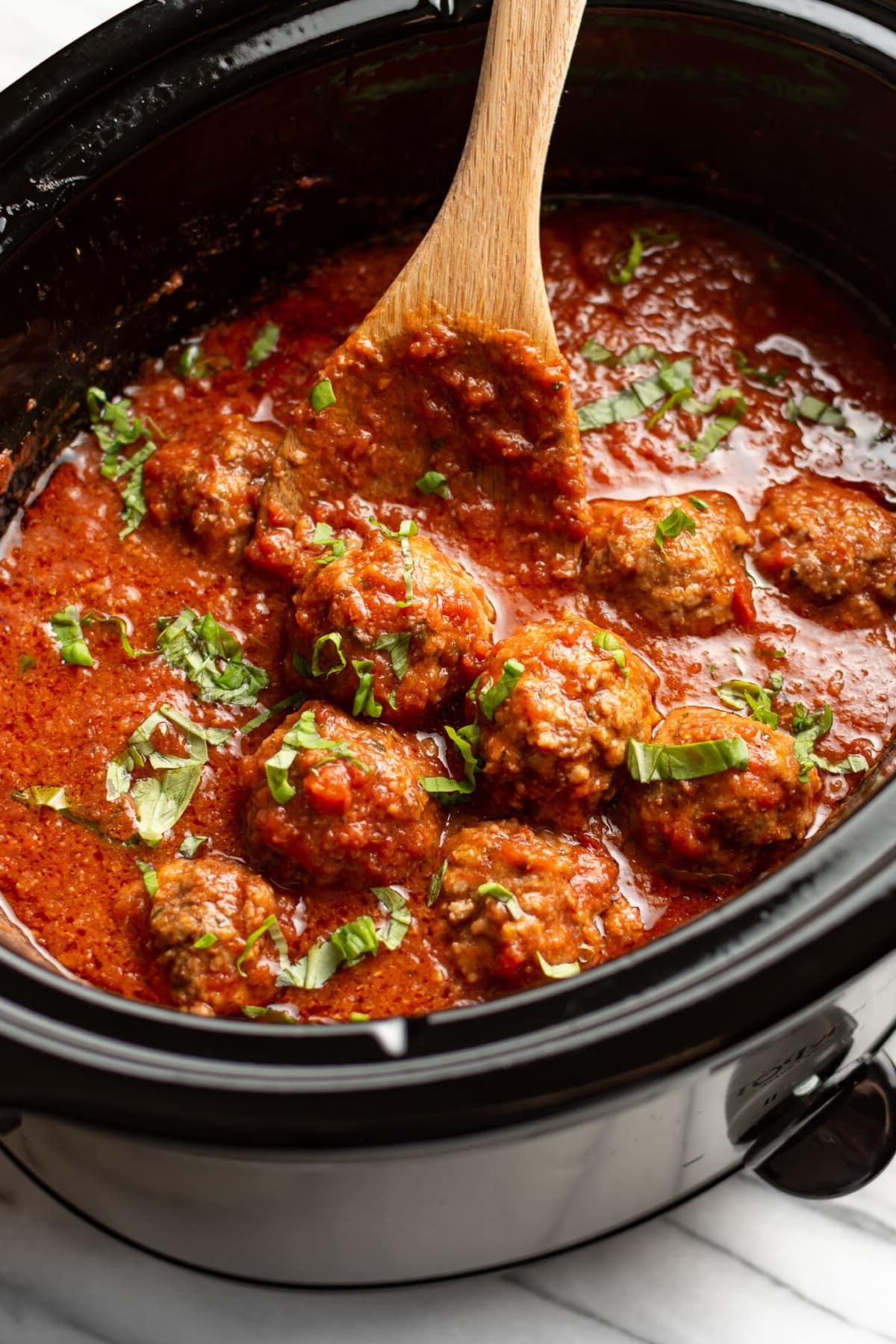 Ein Slow Cooker mit Hackbällchen in Tomatensauce und einem Holzkochlöffel