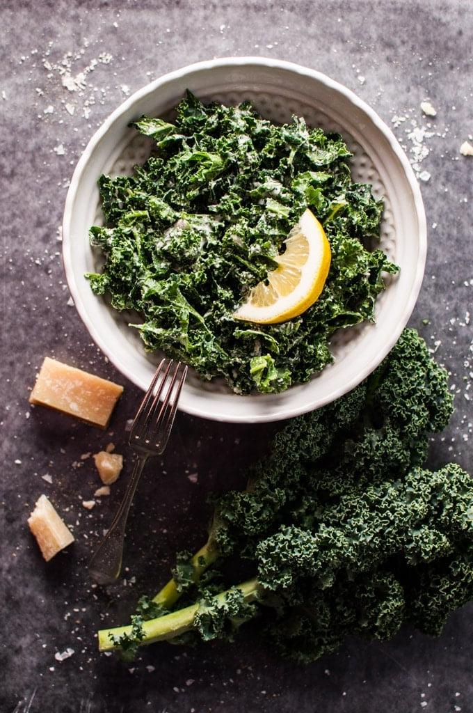 Eine weiße Schale mit Grünkohlsalat, Parmesan, Zitrone und schwarzem Trüffelöl mit einer Gabel