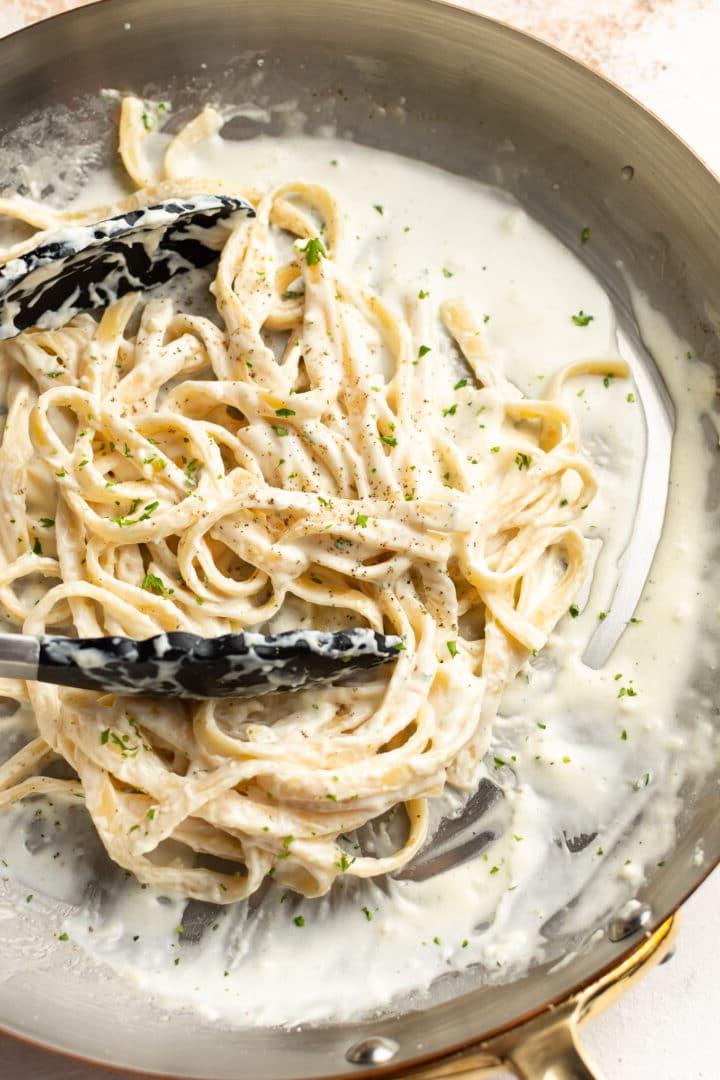 **Schnelle und einfache Alfredo-Soße** 2 a skillet with fettuccine alfredo and serving tongs