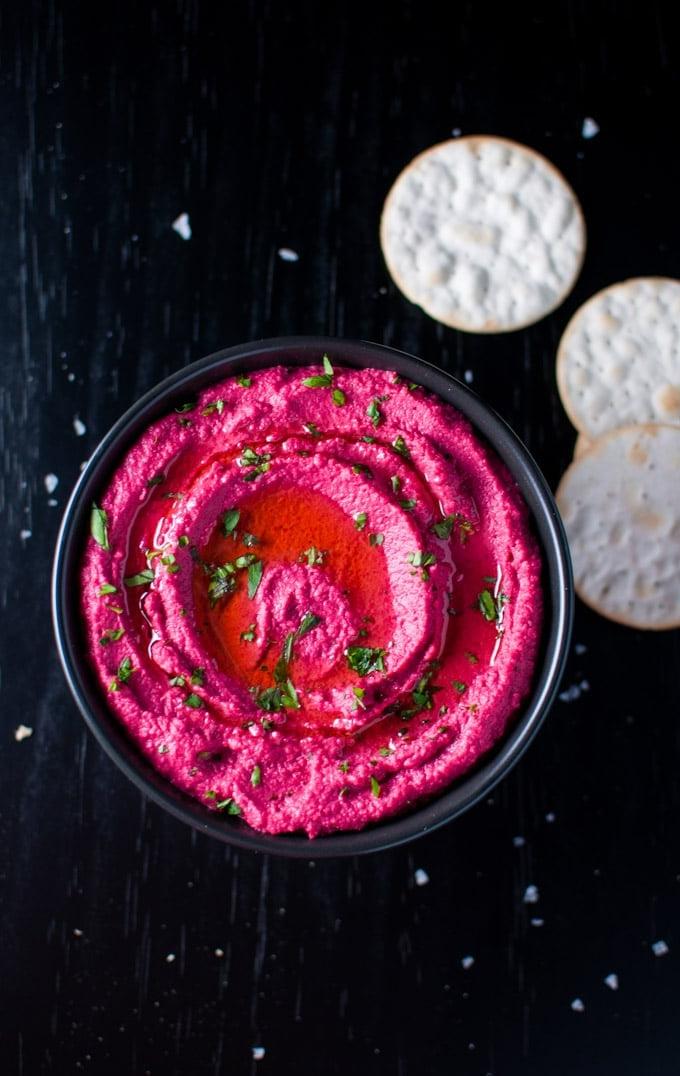 Schwarze Schüssel mit geröstetem Rote Bete Hummus, garniert mit Petersilie und Olivenöl, neben Crackern