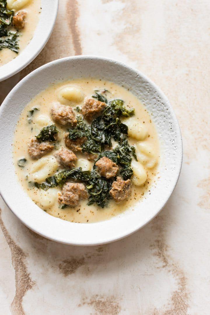 Eine weiße Schüssel mit cremiger Gnocchi-Suppe, Wurst und Grünkohl