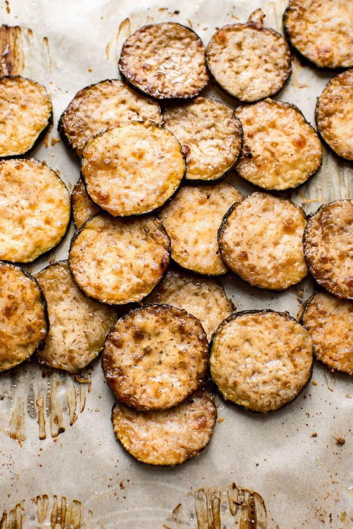 Mehrere gebackene Parmesan-Zucchini-Scheiben auf Backpapier