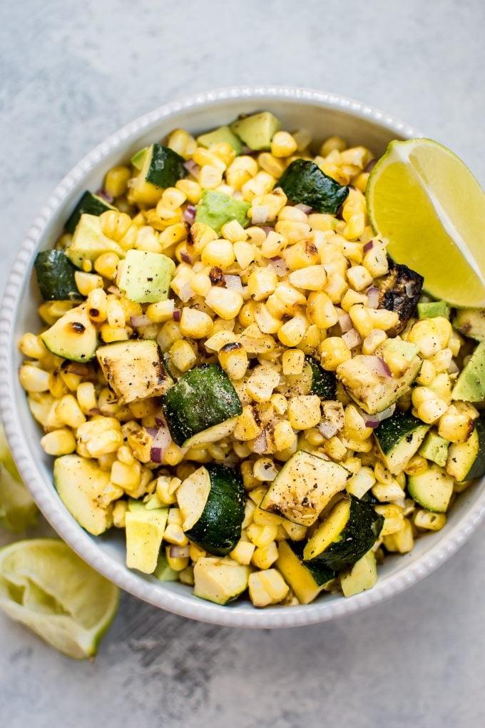 Gegrillter Mais-Zucchini-Salat in einer Schüssel mit Limettenspalte