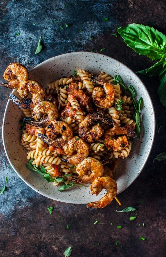 Beige Schüssel mit würziger Pasta und gegrillten Garnelen am Spieß, ansprechend angerichtet.