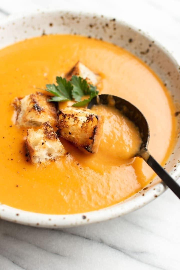 Eine dampfende Schüssel Kartoffel-Lauch-Tomaten-Suppe, garniert mit frischen Croutons und einem Löffel