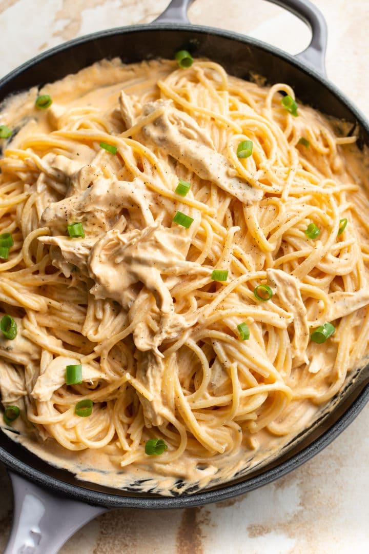 Eine Nahaufnahme von cremiger Buffalo Chicken Pasta mit Soße und Spaghetti in einer großen Pfanne