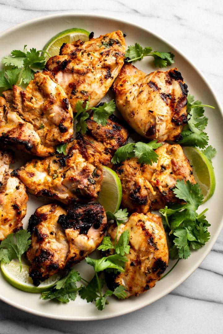 gegrillte Hähnchenschenkel mit Koriander-Limette auf einem Teller mit Limettenspalten und frischem Koriander