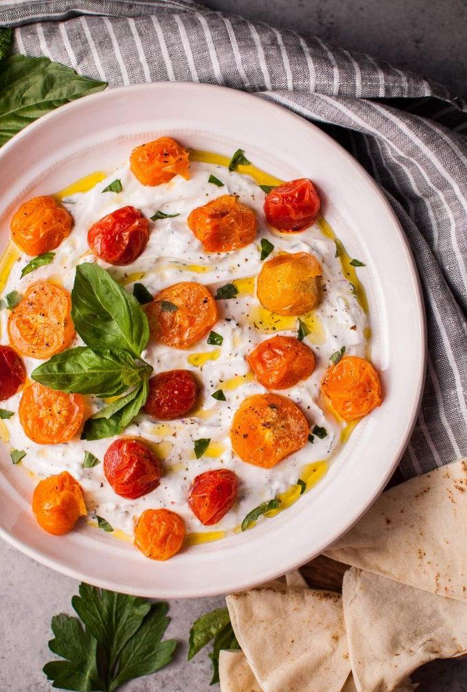 Schüssel mit cremigem griechischem Joghurt-Dip, garniert mit gerösteten Tomaten und frischen Kräutern