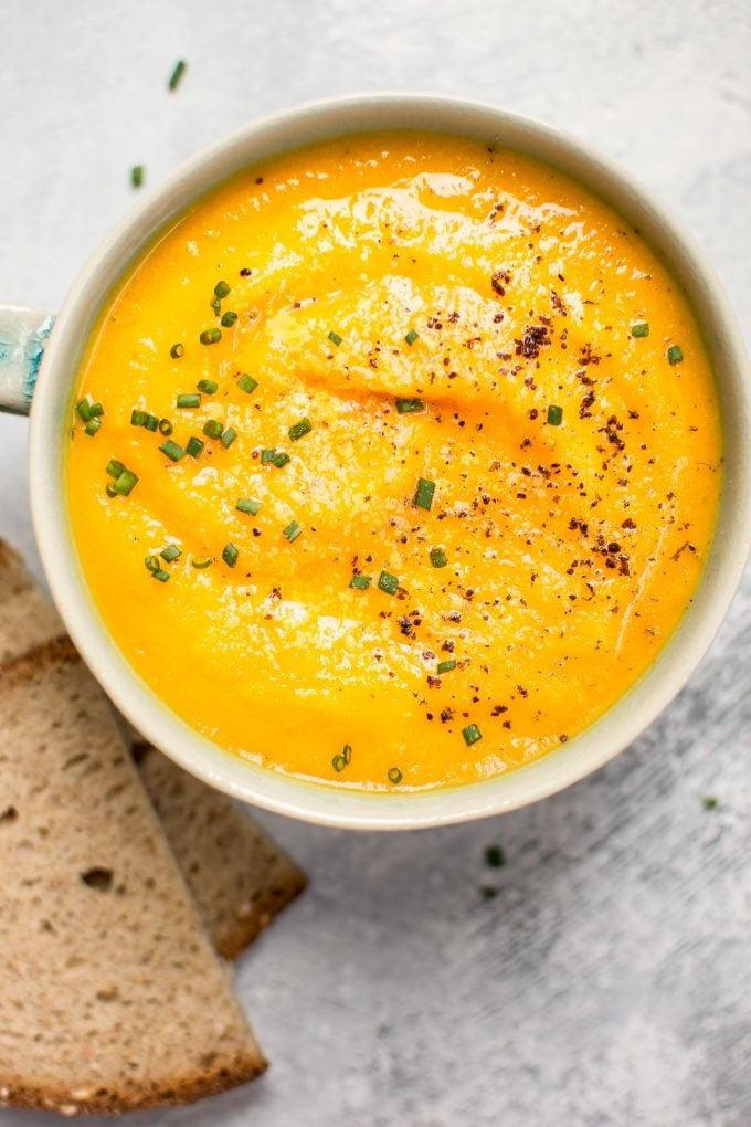 Schüssel mit vegetarischer Eichelkürbis-Karotten-Suppe neben Roggenbrotscheiben