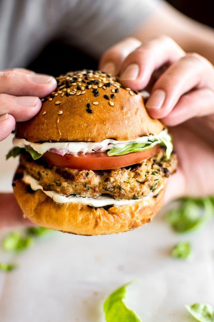 close-up of a man holding a ground turkey burger with mayo, tomato, and lettuce on a sesame bun