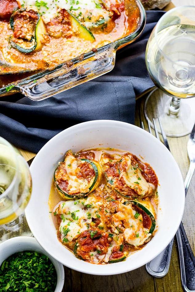 bolognese zucchini lasagna roll-ups in a bowl beside glass of white wine