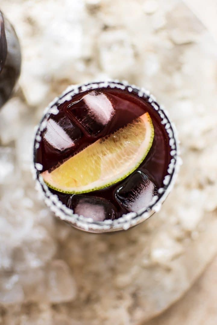Nahaufnahme einer einfachen Schwarzkirsch-Margarita auf Eis mit Limettenspalten in einem Glas