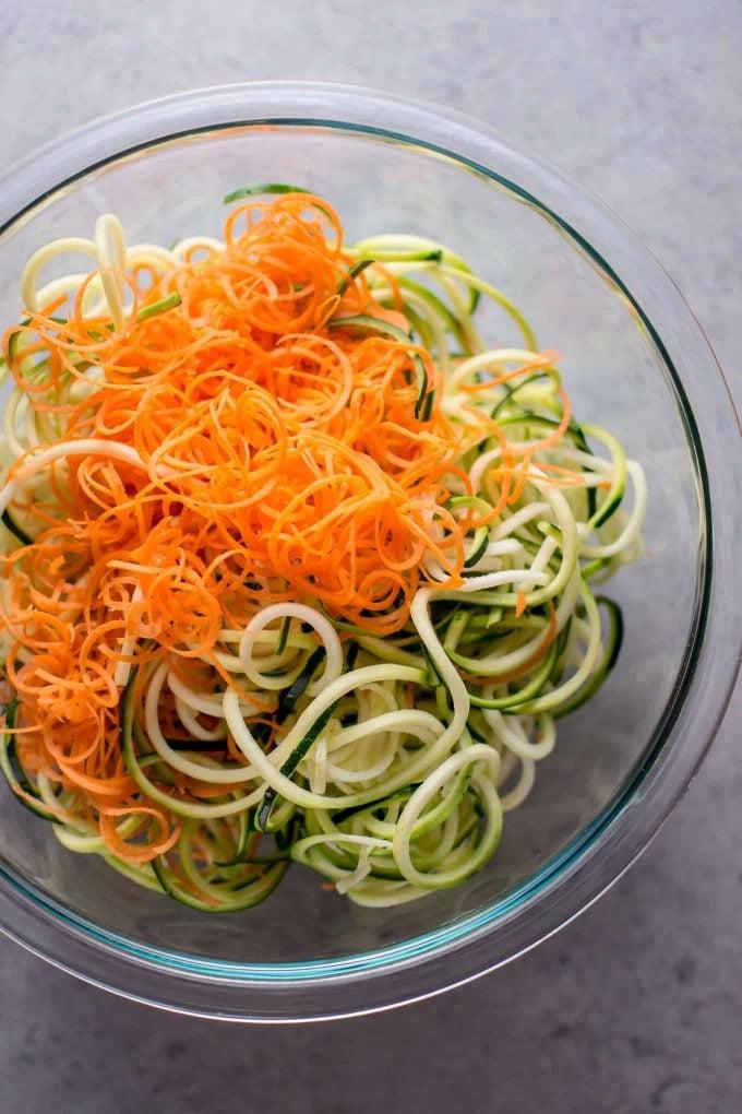 Frisch spiralisierte Zucchini-Nudeln und Karotten in einer eleganten Glasschüssel, bereit zur weiteren Zubereitung.