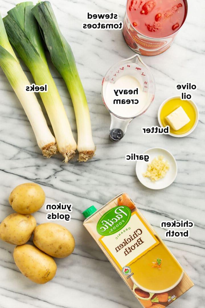 Ausgebreitete Zutaten für die Zubereitung von Kartoffel-Lauch-Tomaten-Suppe auf einer sauberen Küchentheke