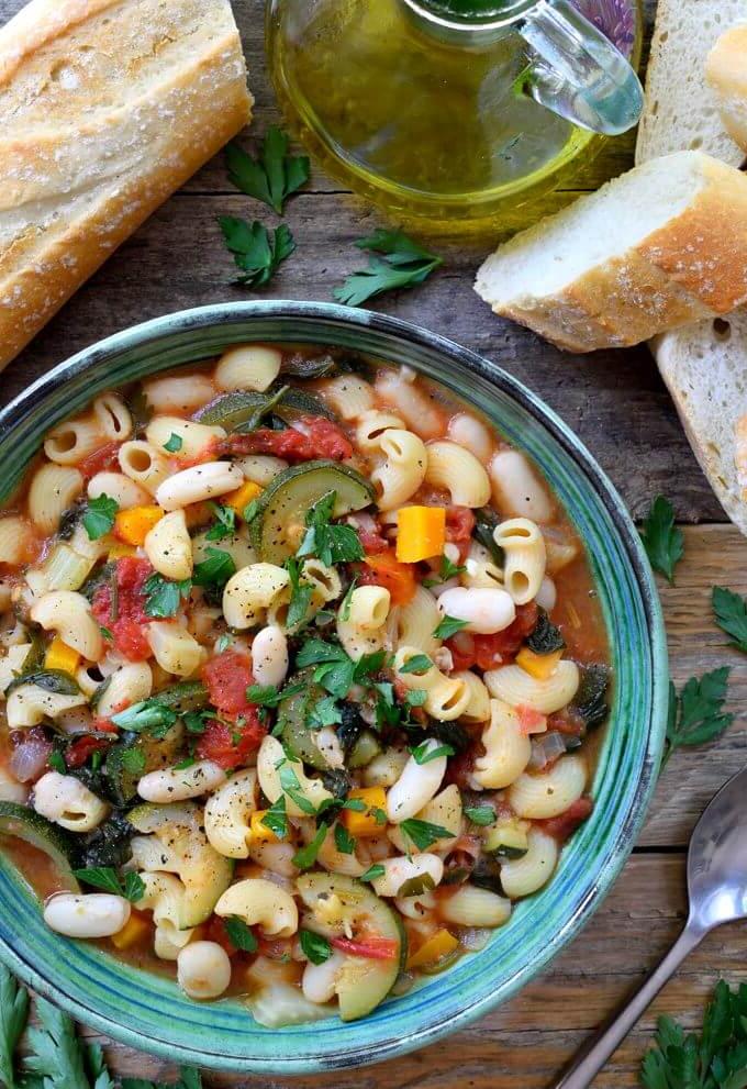a bowl of vegetarian pasta fagioli on wooden surface with slices of bread