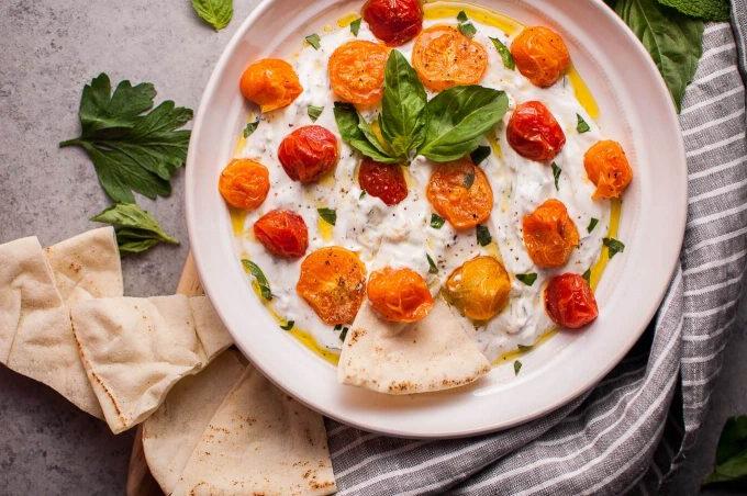 Schüssel mit sommerlichem griechischem Joghurt-Dip mit gerösteten kleinen Tomaten, appetitlich angerichtet mit Pita-Brot-Scheiben