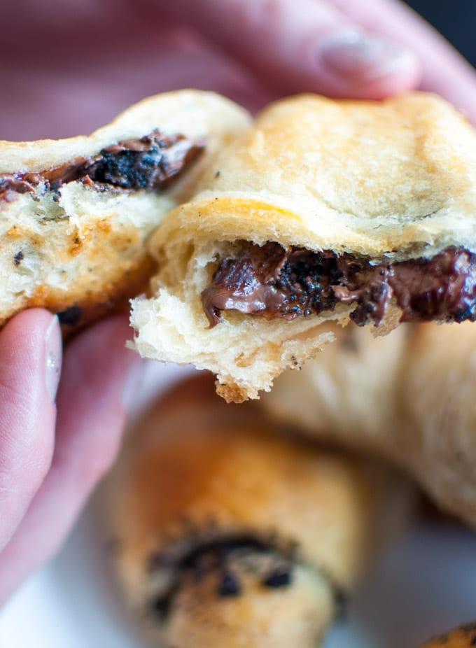 Oreo- und Nutella-gefüllte Hörnchen 3 Nahaufnahme einer Hand, die ein warmes, frisch gebackenes Nutella- und Oreo-gefülltes Hörnchen hält, mit leicht geschmolzener Schokoladenfüllung