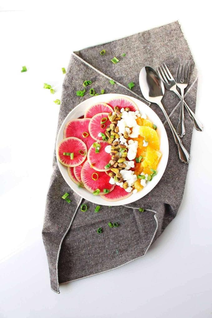 watermelon, radish, and orange salad on a plate beside forks and spoon