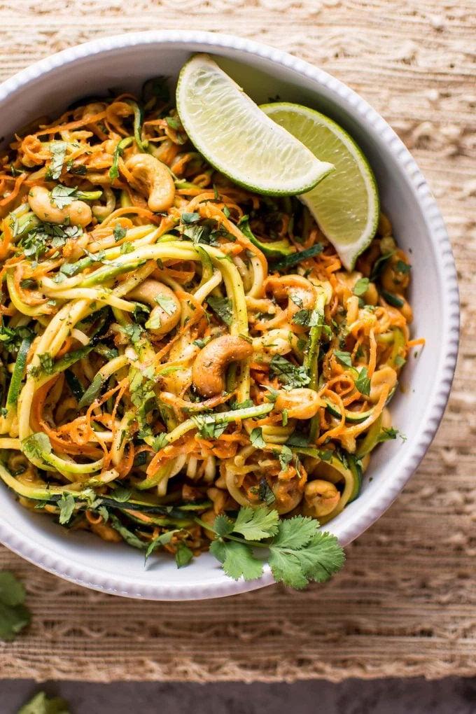 Nahaufnahme einer Portion 15-Minuten-Knoblauch-Limetten-Cashew-Zoodles in einer Schüssel, detailreich präsentiert mit Limettenspalten im Hintergrund.