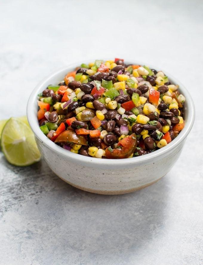 Weiße Schüssel mit Mais- und Schwarze-Bohnen-Salat neben Limettenspalten