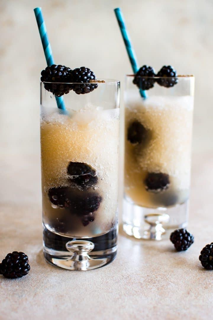 Zwei hohe klare Gläser mit gefrorenem Riesling und frischen Brombeeren mit blauen Strohhalmen