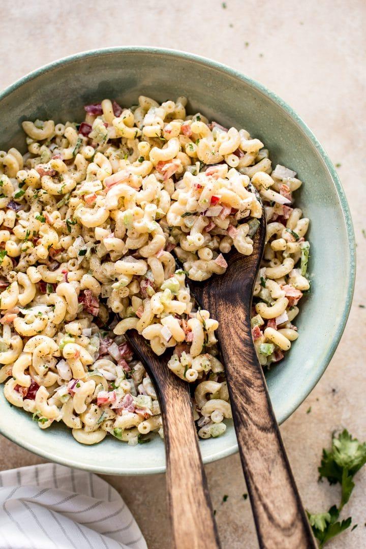 creamy macaroni salad in a teal bowl with wooden salad utensils