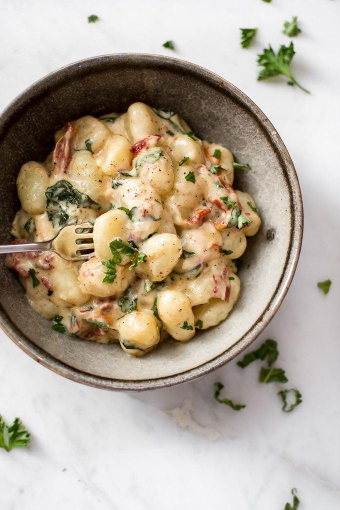 Cremige Gnocchi mit sonnengetrockneten Tomaten und Basilikum 4 Nahaufnahme von Gnocchi mit getrockneten Tomaten und Basilikum in einer Schüssel mit einer Gabel