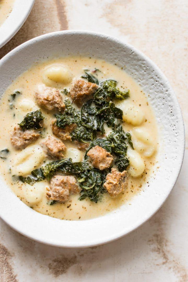 Weiße Schüssel mit einfacher und cremiger Gnocchi-Suppe mit Grünkohl und Wurst