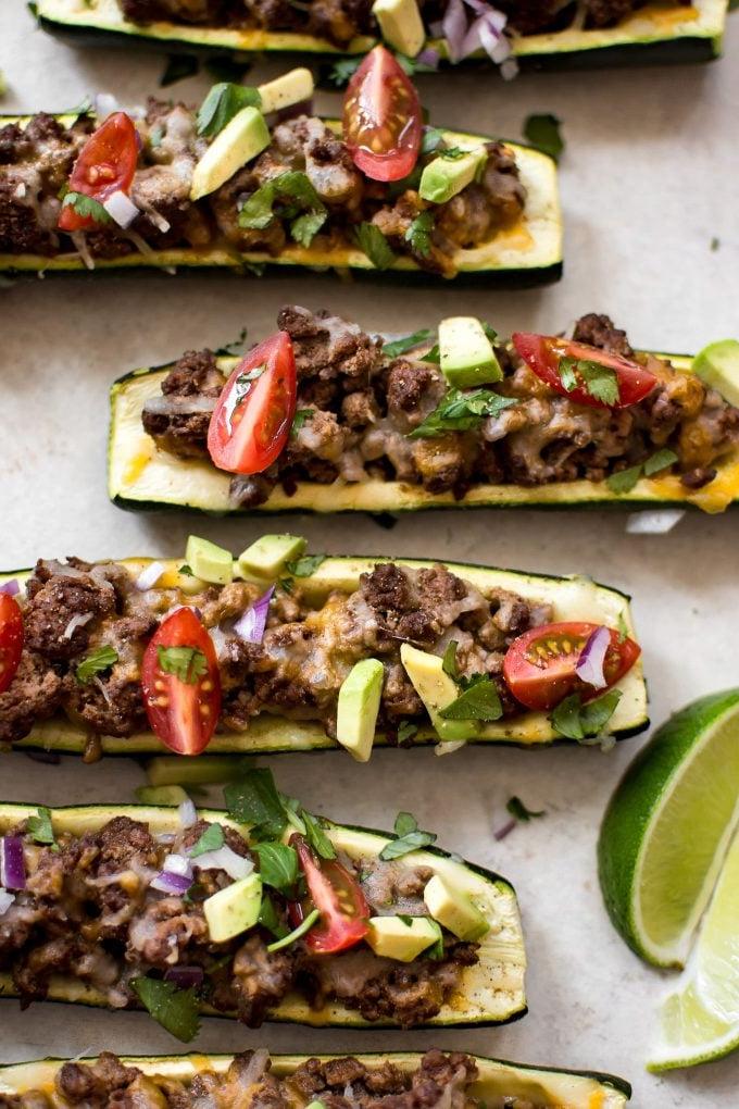 Taco-Zucchini-Boote belegt mit Hackfleisch, Käse, Avocado und Tomaten.