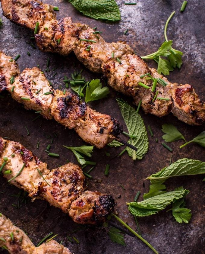Nahaufnahme von drei gegrillten vietnamesischen Zitronengras-Schweinefilet-Spießen mit Minzblättern