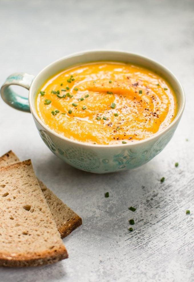 Suppentasse mit vegetarischer Eichelkürbis-Karotten-Suppe neben Roggenbrotscheiben