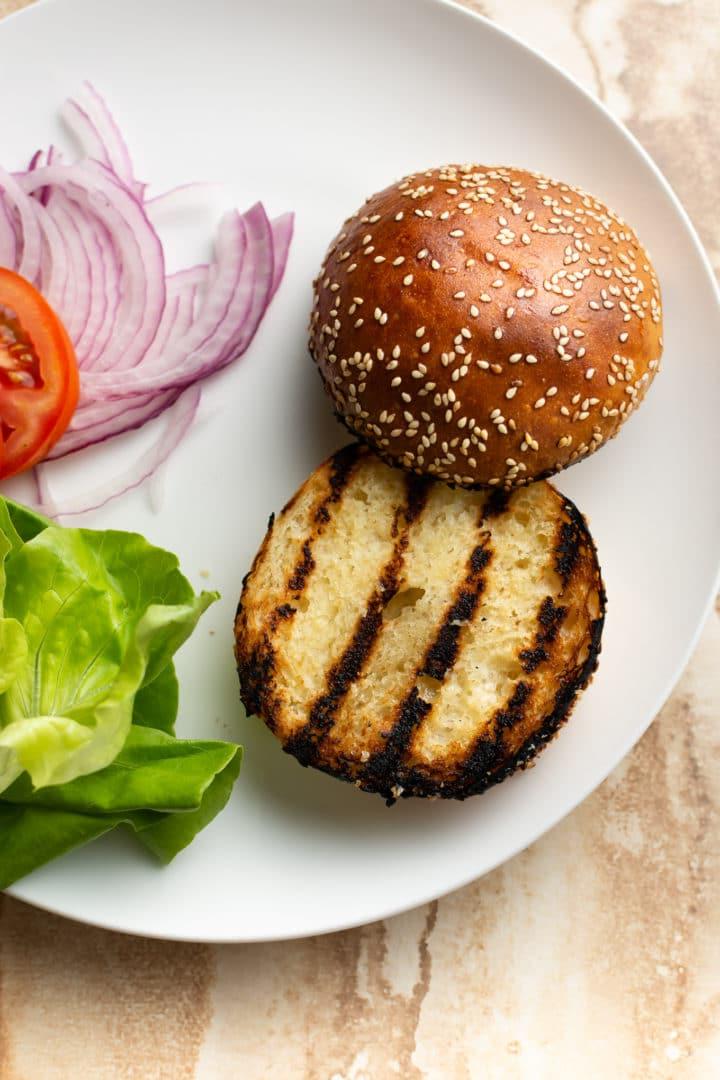 Hausgemachte Hähnchen-Hackfleisch-Burger-Beläge auf einem Teller (Brötchen, Salat, Tomate, rote Zwiebeln)