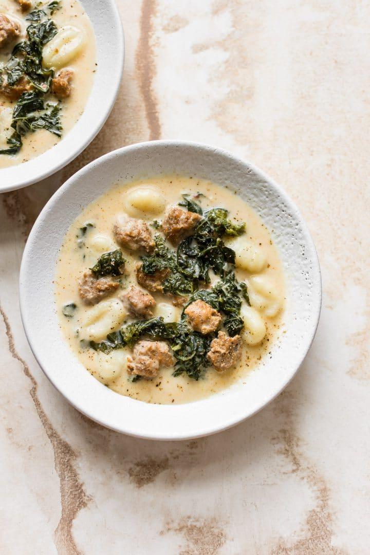 Zwei weiße Schüsseln mit cremiger Wurstsuppe mit Gnocchi und Grünkohl