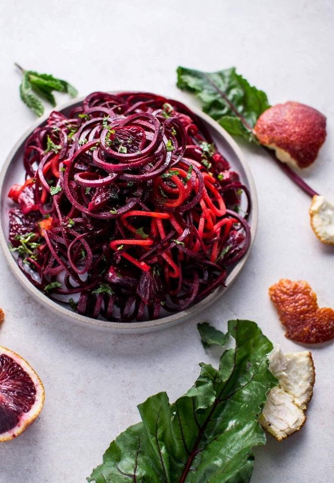 Schale mit veganem Rote-Bete-Blutorangen-Salat neben Orangenschalen und Rote-Bete-Blättern