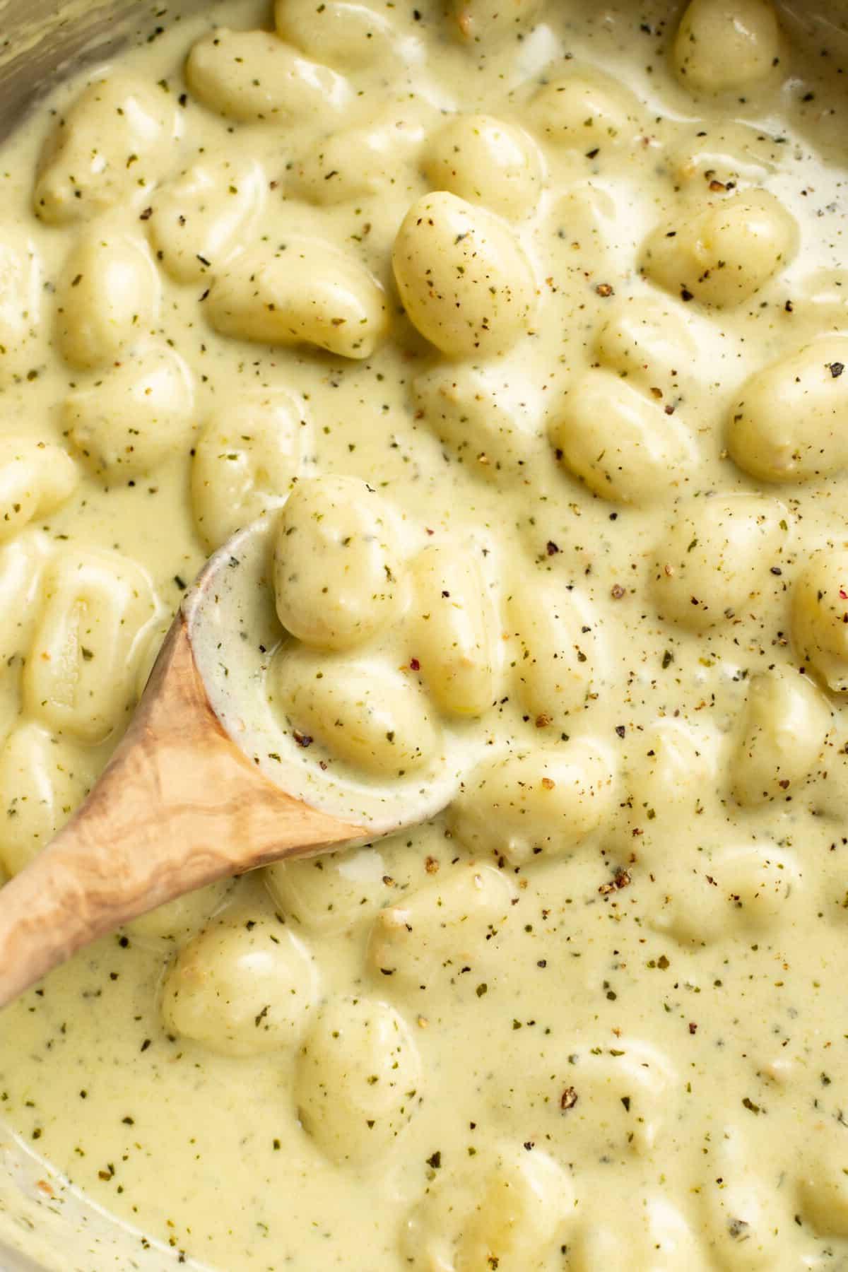 Nahaufnahme einer Pfanne mit cremigen Pesto Gnocchi und einem Holzlöffel, der die cremige Textur zeigt.