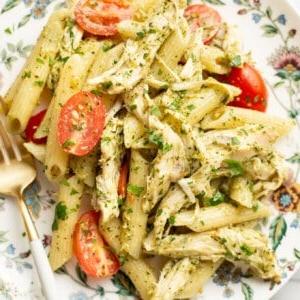 Ein appetitlich angerichteter Teller Hähnchen-Pesto-Nudelsalat mit einer Gabel.