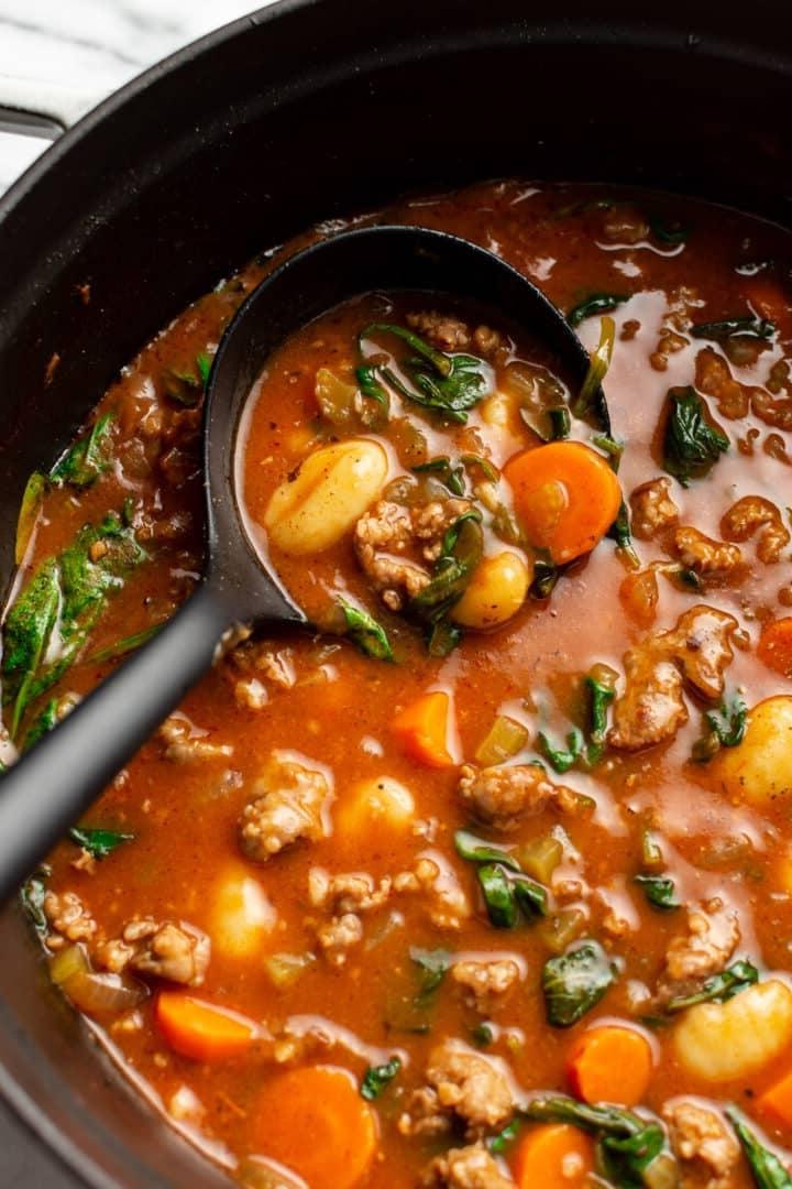 Eine Suppenkelle in einem Topf mit Wurst-Gnocchi-Suppe