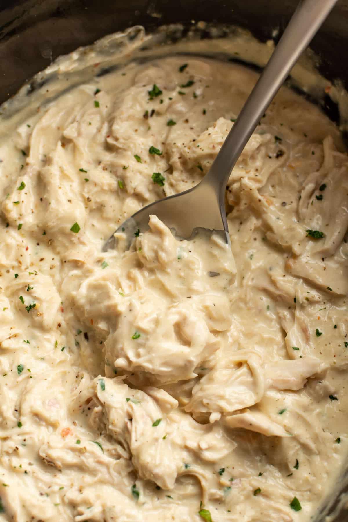 Nahaufnahme eines Slow Cookers mit italienischem Hähnchen und einem Löffel