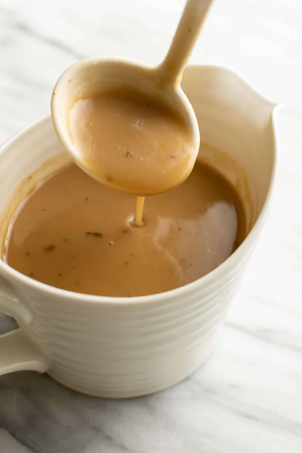 a gravy boat with brown gravy and a serving spoon