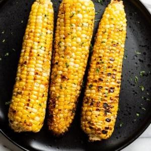 3 gegrillte Maiskolben auf einem schwarzen Teller