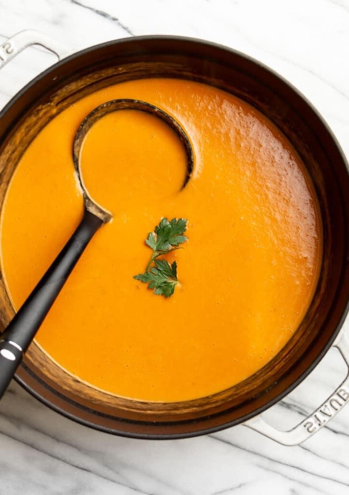 Ein großer Topf mit cremig pürierter Tomaten-, Lauch- und Kartoffelsuppe, mit einer Schöpfkelle darin