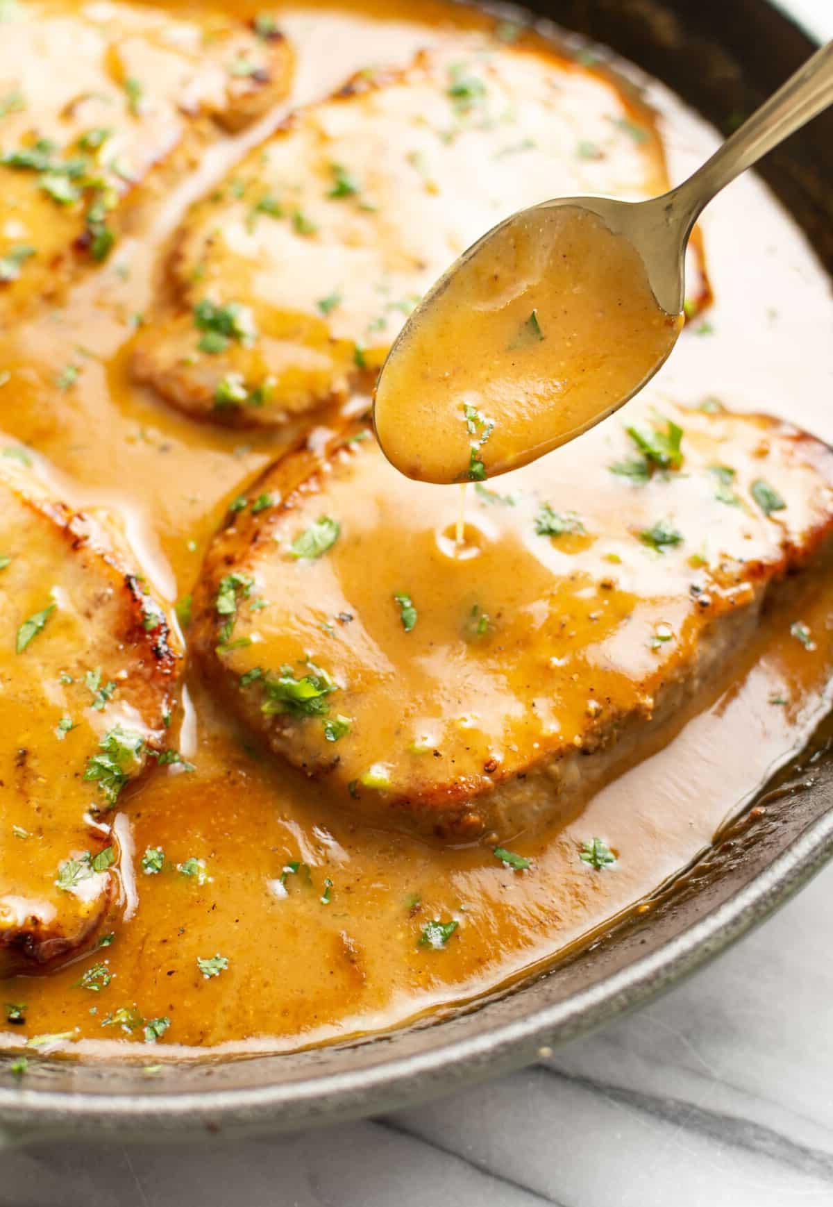 Eine Pfanne mit Honig-Senf-Schweinekoteletts und einem Servierlöffel