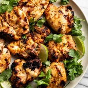 gegrillte Hähnchenschenkel mit Koriander-Limette auf einem Teller mit Limettenspalten und frischem Koriander